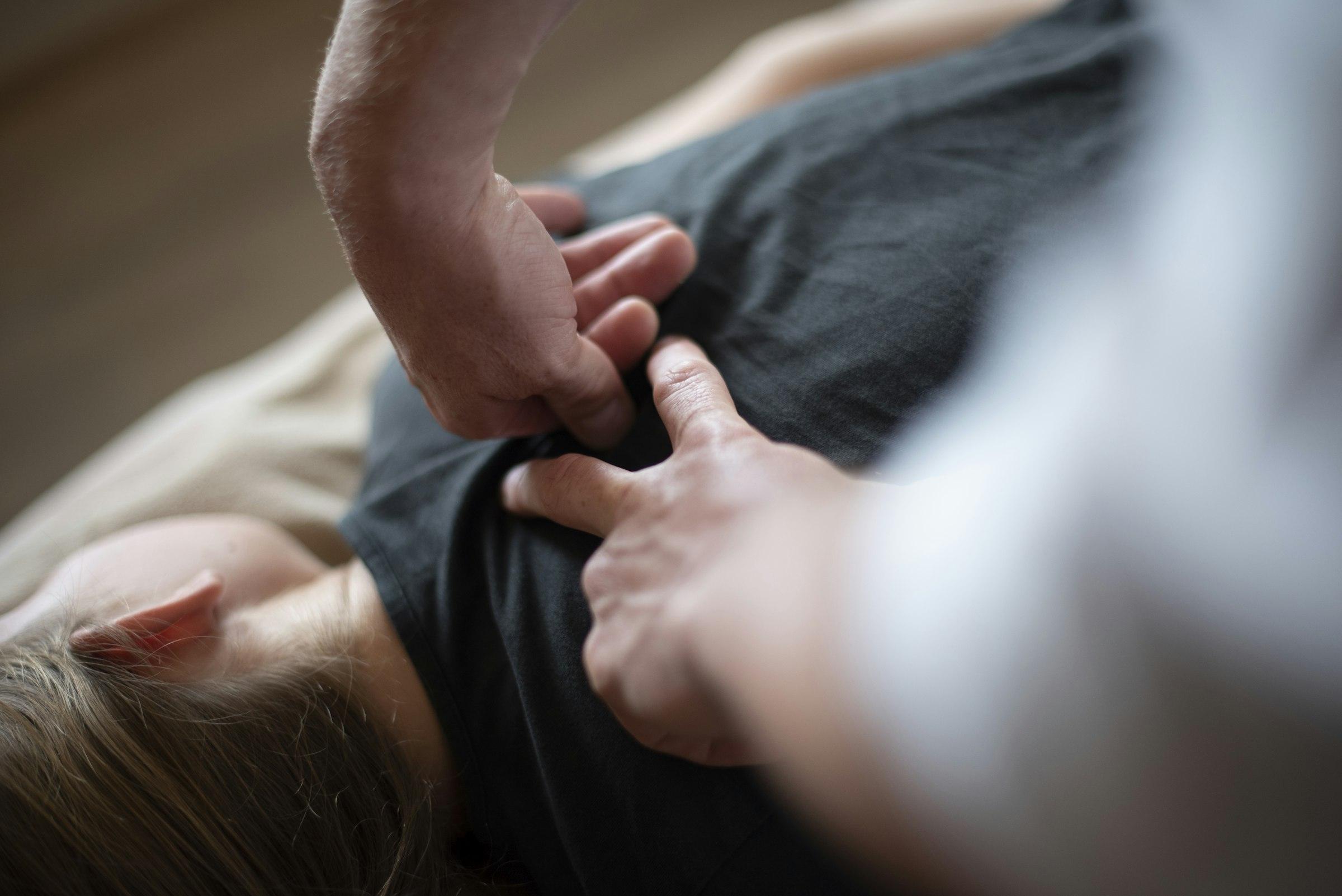 Hände einer Therapeutin am Rücken eines Patienten, heller Behandlungsraum